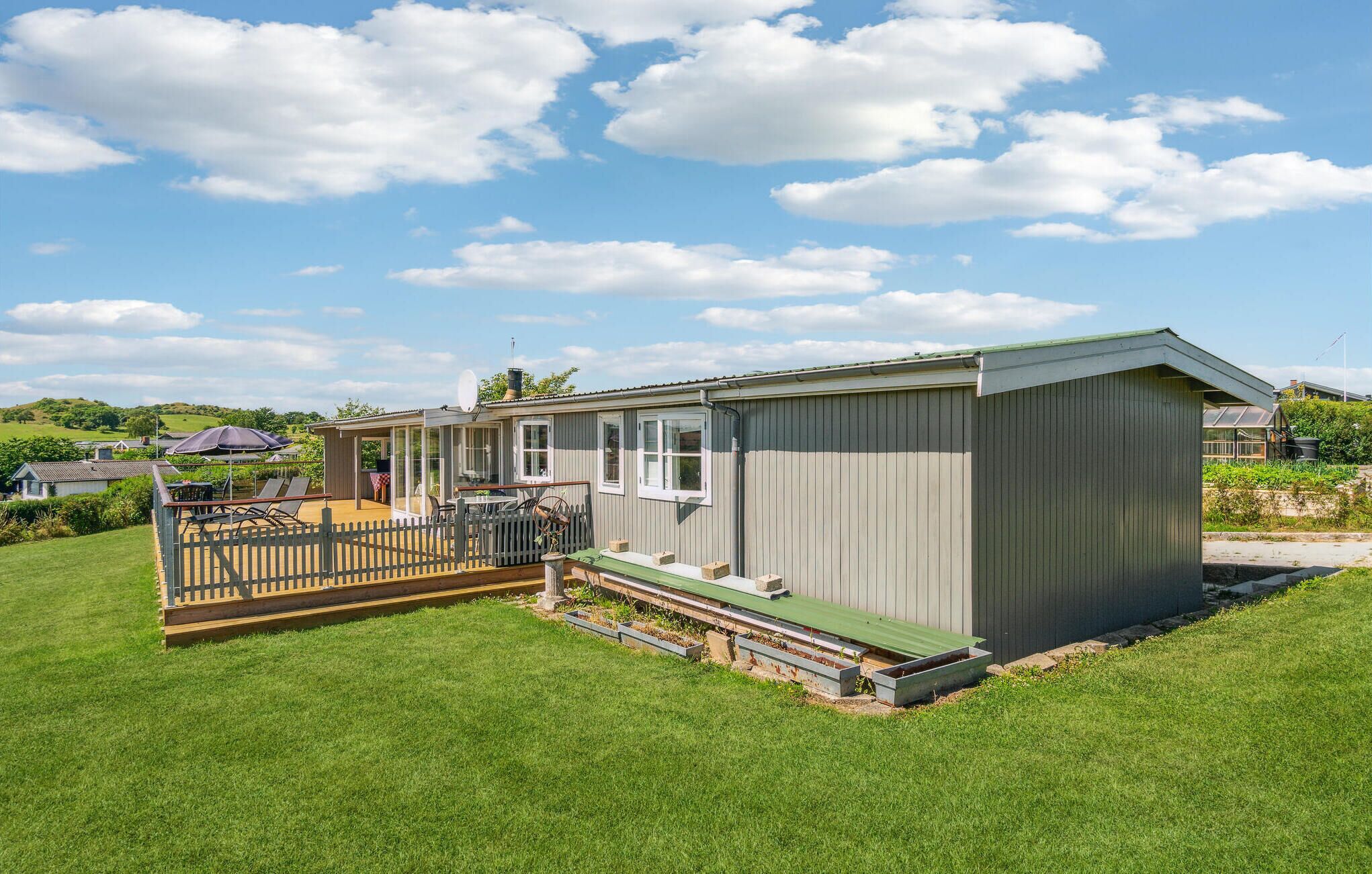 A single-story mobile home with a fenced deck, a satellite dish, and a green roof.