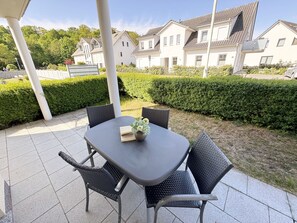 An outdoor patio with a table and chairs, surrounded by neatly trimmed hedges and a row of houses in the background.