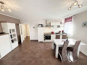 A modern kitchen with white cabinets, a dining area with a white table and chairs, and a clock on the wall.
