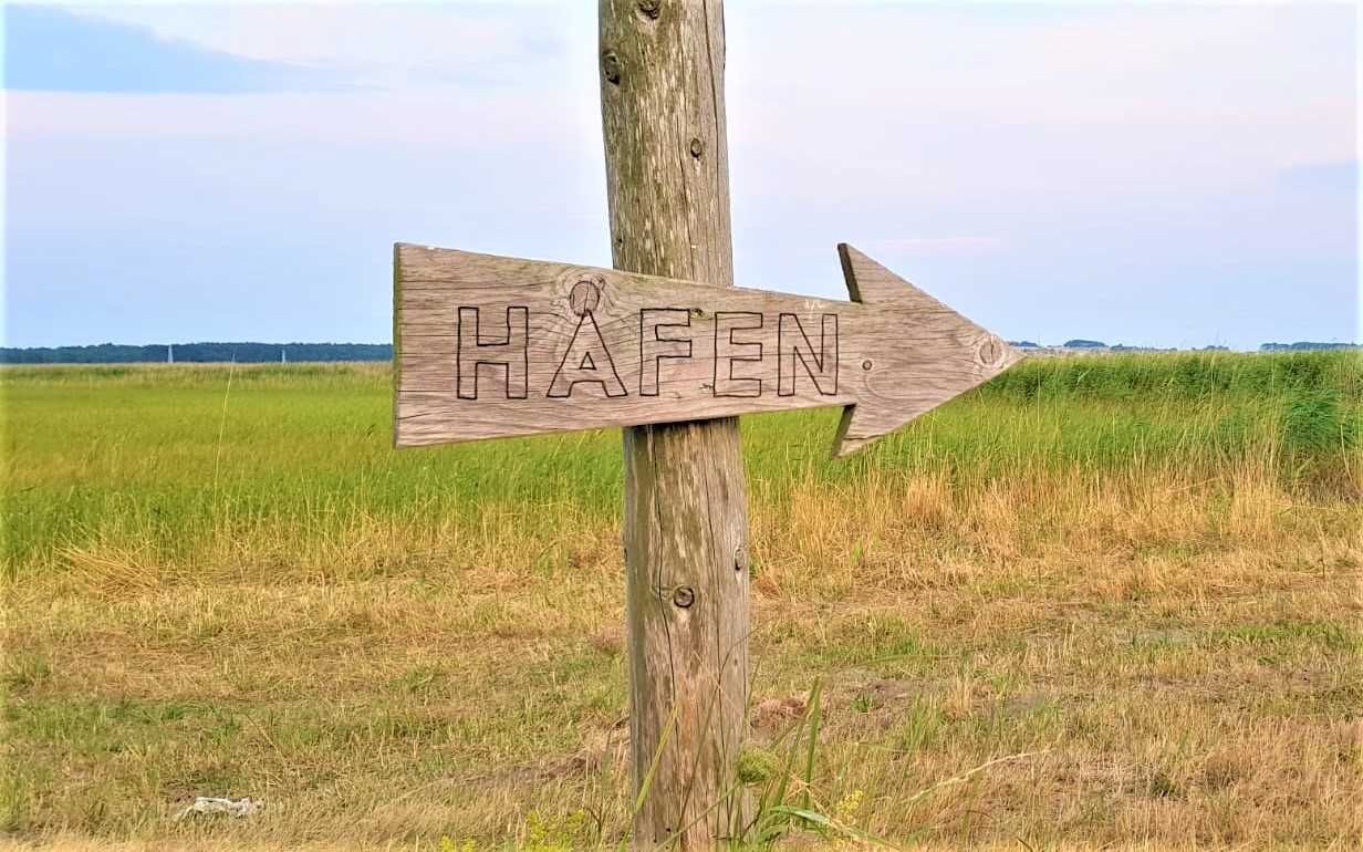 Uma placa de madeira indicadora com a palavra 'HAFEN' apontando para a direita.