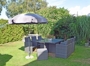 An outdoor patio with a table and chairs, a large umbrella, and lush greenery in the background.
