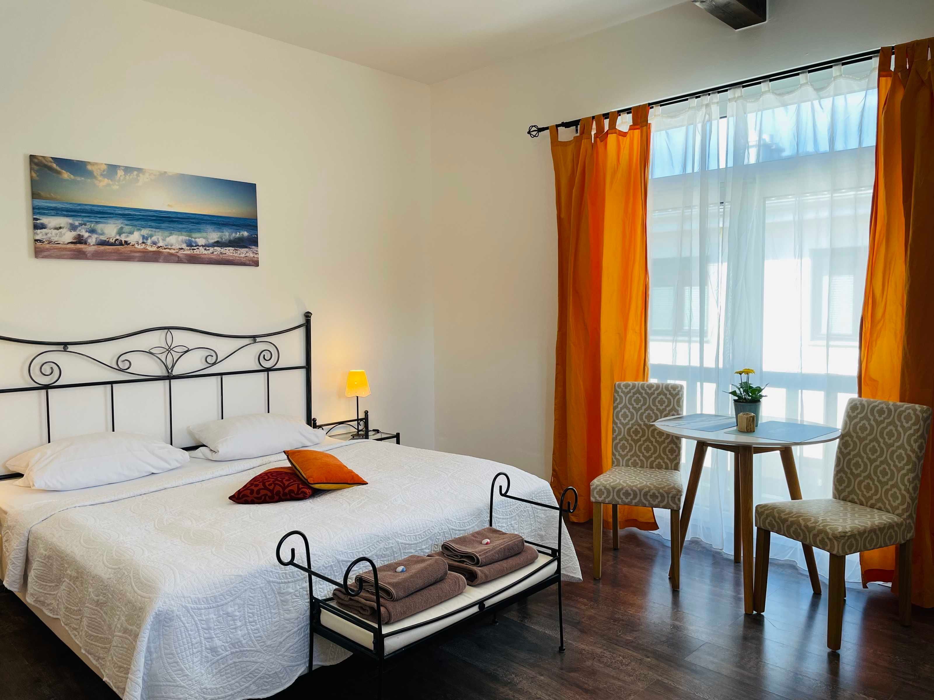 Ein Hotelzimmer mit einem Bett, einem Nachttisch mit Lampe, einem Sessel, einem kleinen Tisch mit Pflanze und einem Fenster mit Vorhängen.