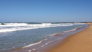 Una playa con olas, cielo despejado y orilla arenosa.