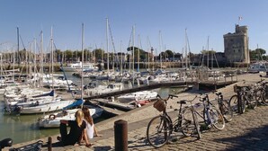 Un puerto deportivo con numerosas embarcaciones amarradas, una estructura similar a un castillo al fondo y bicicletas estacionadas a lo largo del muelle.