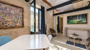 Un intérieur moderne avec une grande table blanche, des chaises bleues, une œuvre d’art en vitrail, un téléviseur fixé au mur et une cheminée.
