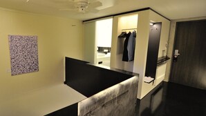 Ein modernes Hotelzimmer mit Schwarz-Weiß-Farbgestaltung, einem Deckenventilator, einem Bild an der Wand und Blick ins Badezimmer.