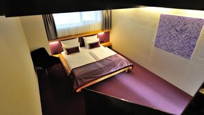 Ein kleines, kompaktes Zimmer mit einem Einzelbett, einem Sessel und einem kleinen Tisch.