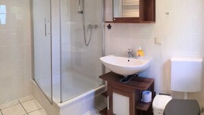 A modern bathroom with a glass-enclosed shower, a white sink, and a wooden vanity. - Vacation cottage Robert, Germany (Bergen auf Rügen)
