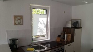 A compact kitchen with a window, a microwave, a kettle, and basic appliances. - Vacation cottage Robert, Germany (Bergen auf Rügen)
