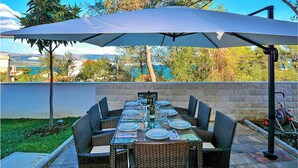 Un área de comedor al aire libre con una mesa dispuesta para seis personas, rodeada de sillas de mimbre y protegida por una sombrilla grande.