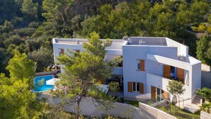 Una casa moderna de dos pisos con piscina, rodeada de árboles y un muro de piedra.
