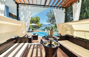 Een terras buiten met rieten meubilair, een zwembad en uitzicht op zee.