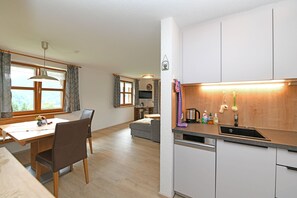 Ett modernt kök med diskmaskin, en matplats med bord och stolar samt ett vardagsrum med soffa och TV.