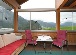 Ett rum med ett träpanelat tak, en rödrandig soffa, två röda stolar, ett litet bord och stora fönster med utsikt över bergen.