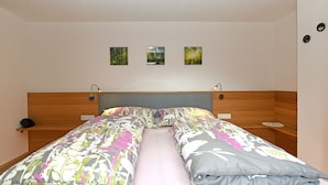 A double bed with floral bedding, a wooden headboard, bedside tables, and three framed pictures on the wall.