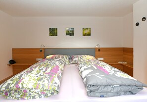 A double bed with floral bedding, a wooden headboard, bedside tables, and three framed pictures on the wall.