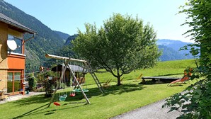 A house with a swing set, a tree, and a view of mountains.