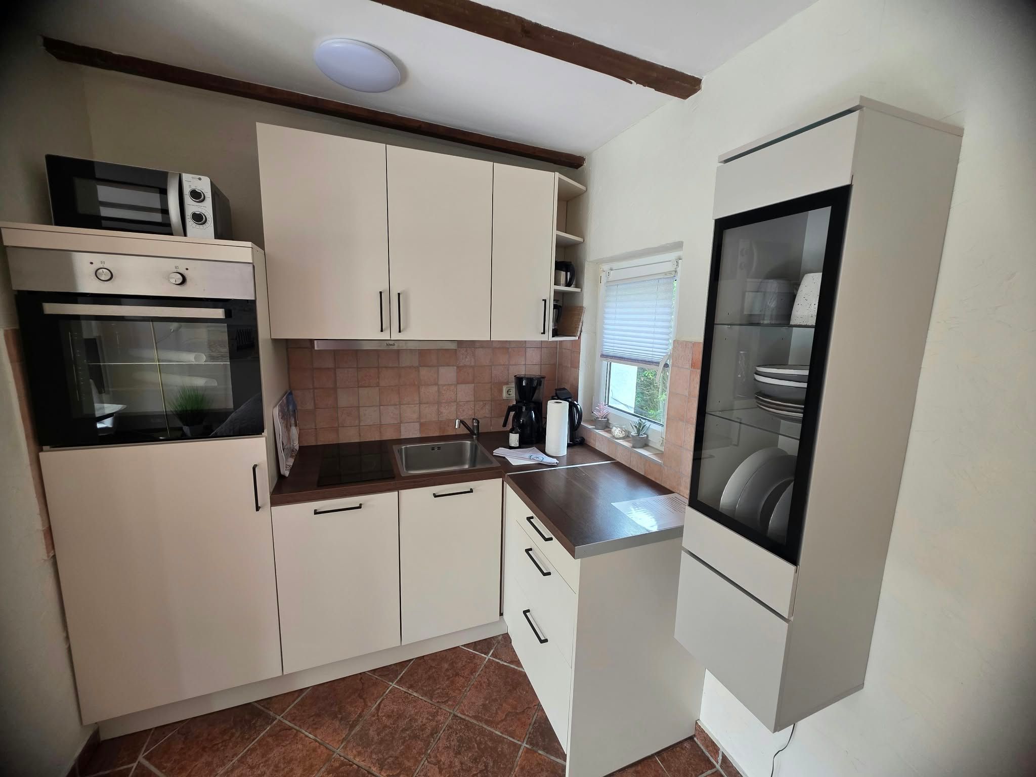 A compact kitchen with white cabinets, a built-in oven, a coffee maker, and a dishwasher.