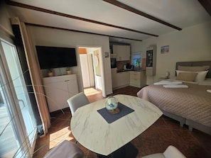Habitación de hotel compacta con cama, mesa de comedor, zona de cocina y televisor.
