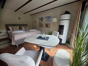 A hotel room with a bed, a round table, two chairs, a fireplace, and a large window.