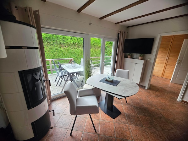 A modern kitchen with a dining area, a TV mounted above the cabinets, and a sliding glass door leading to a patio with a view of greenery.
