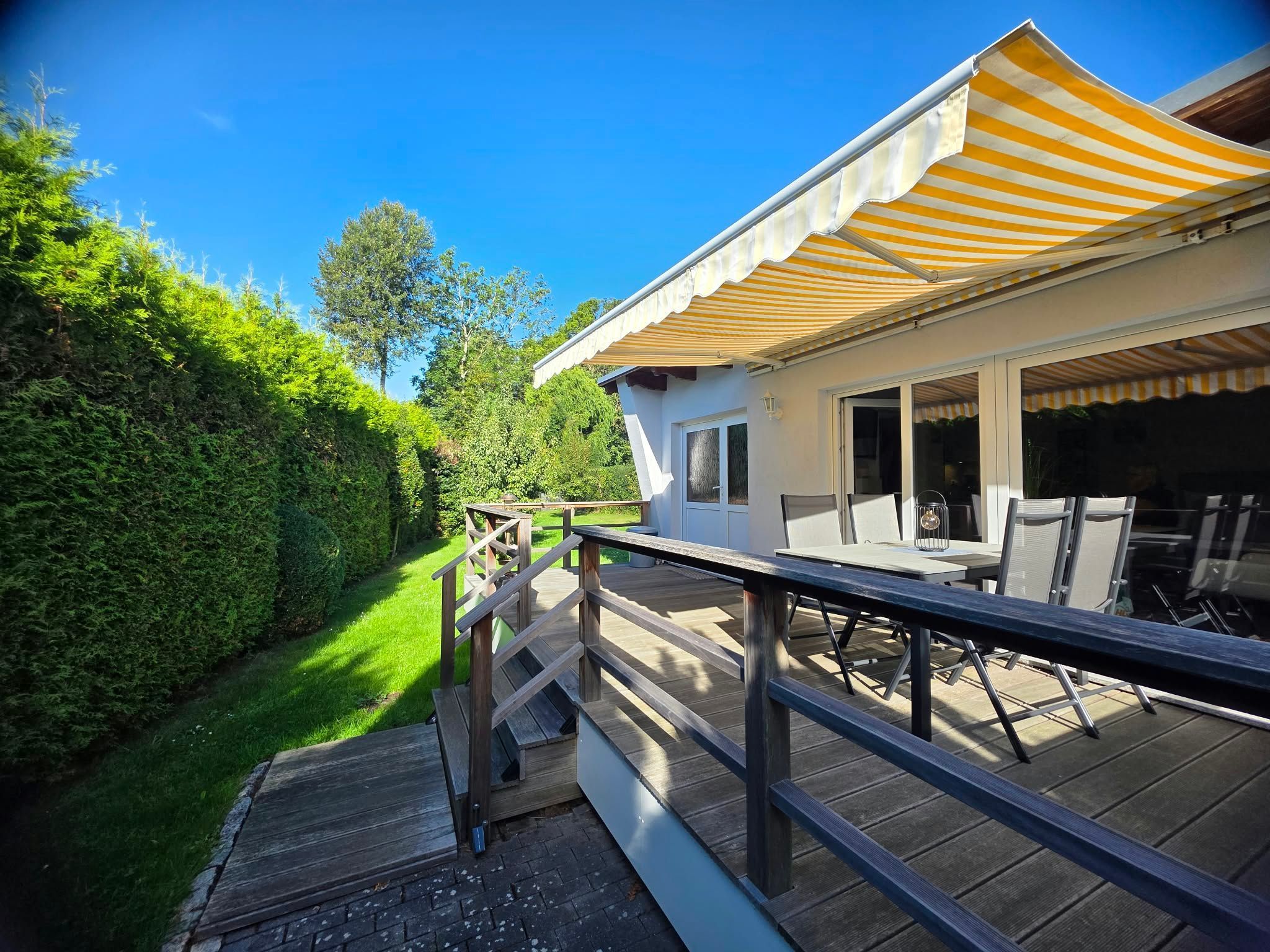 Une terrasse en bois avec des meubles d’extérieur, un patio couvert et une vue sur un jardin luxuriant.
