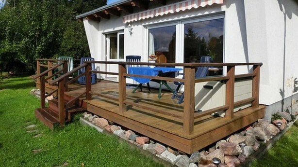 Una casa con terraza de madera, un comedor con mesa y sillas, y un ventanal grande.