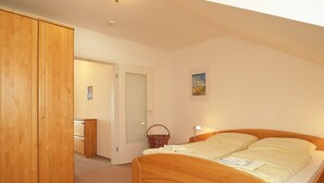 Ein Schlafzimmer mit einem hölzernen Bett, einem Kleiderschrank, einer Tür, einer Wandleuchte und einem gerahmten Bild.