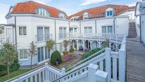 Ein mehrgeschossiges Wohngebäude mit rotem Ziegeldach, weißen Außenwänden und einem Balkon mit weißen Geländern.