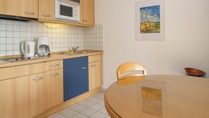 Eine Küche mit Holzausstattung, einer Mikrowelle, einer Kaffeemaschine und einem Esstisch mit einem Stuhl.