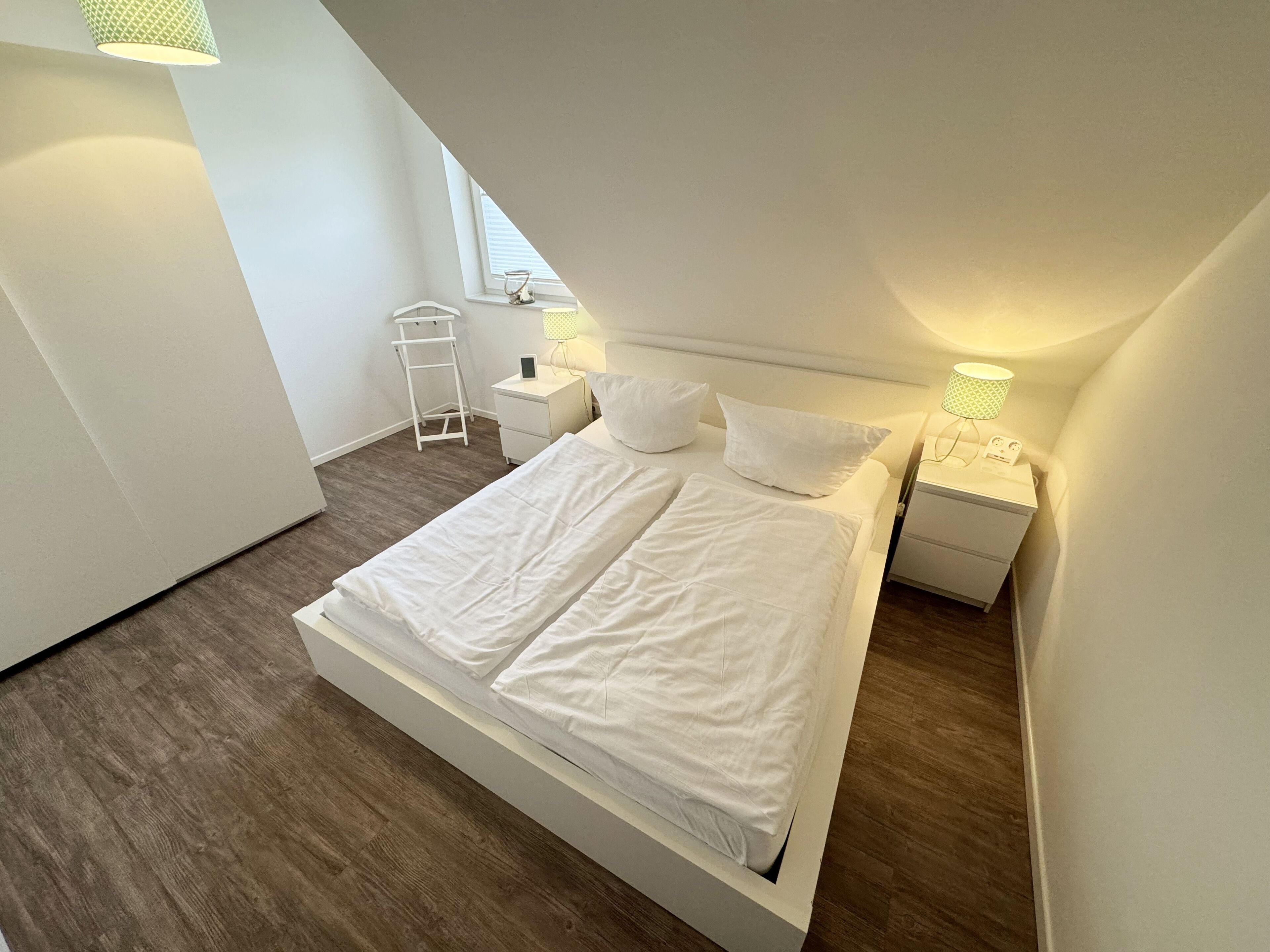 Une chambre moderne avec un grand lit, deux tables de chevet, une commode, une échelle et une fenêtre avec des stores.