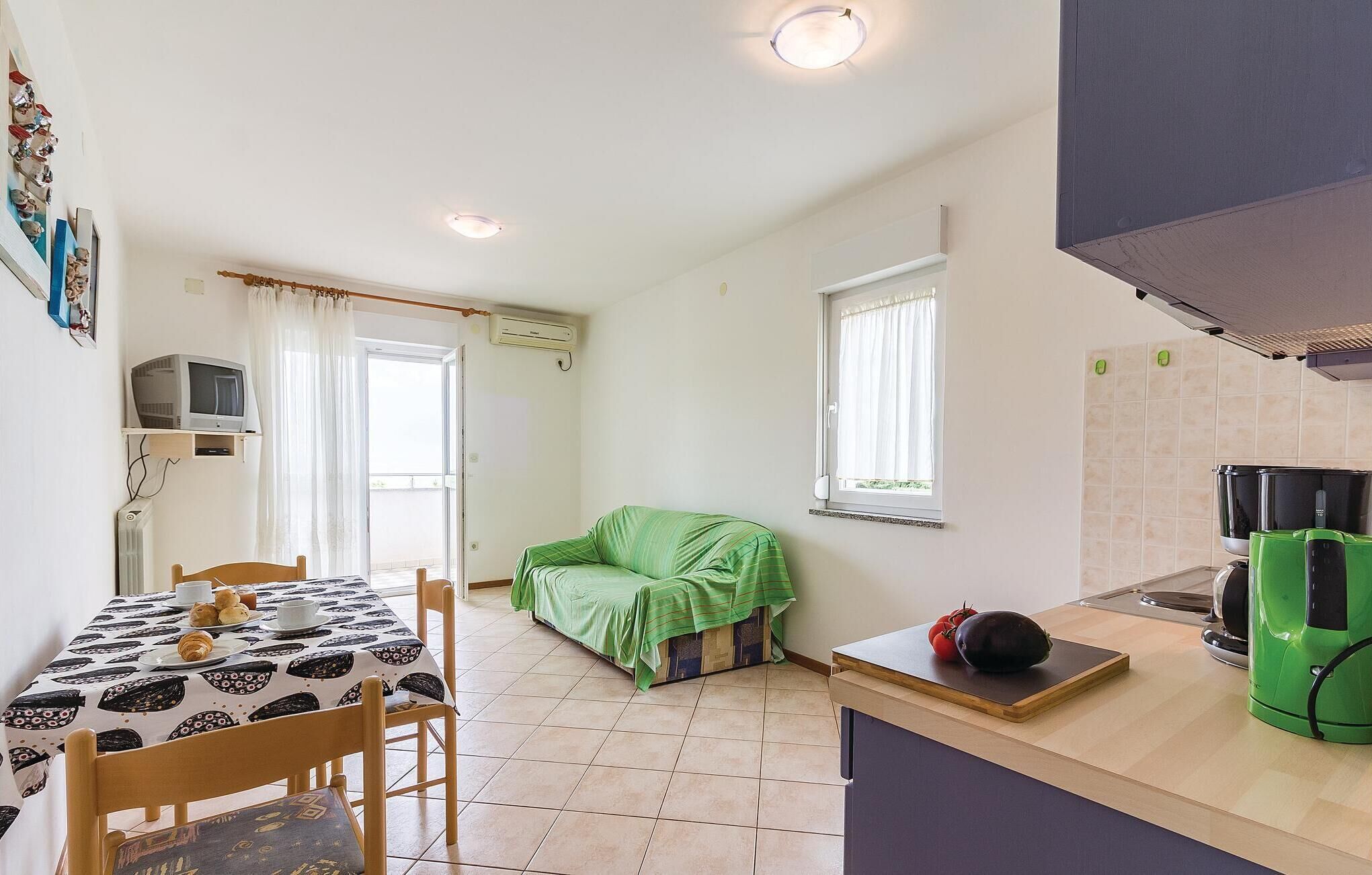 A compact kitchen with a dining area, a green-covered sofa, and a coffee machine.
