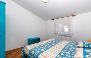 Une chambre à coucher avec un lit, une fenêtre avec des rideaux, un radiateur et une armoire bleue.