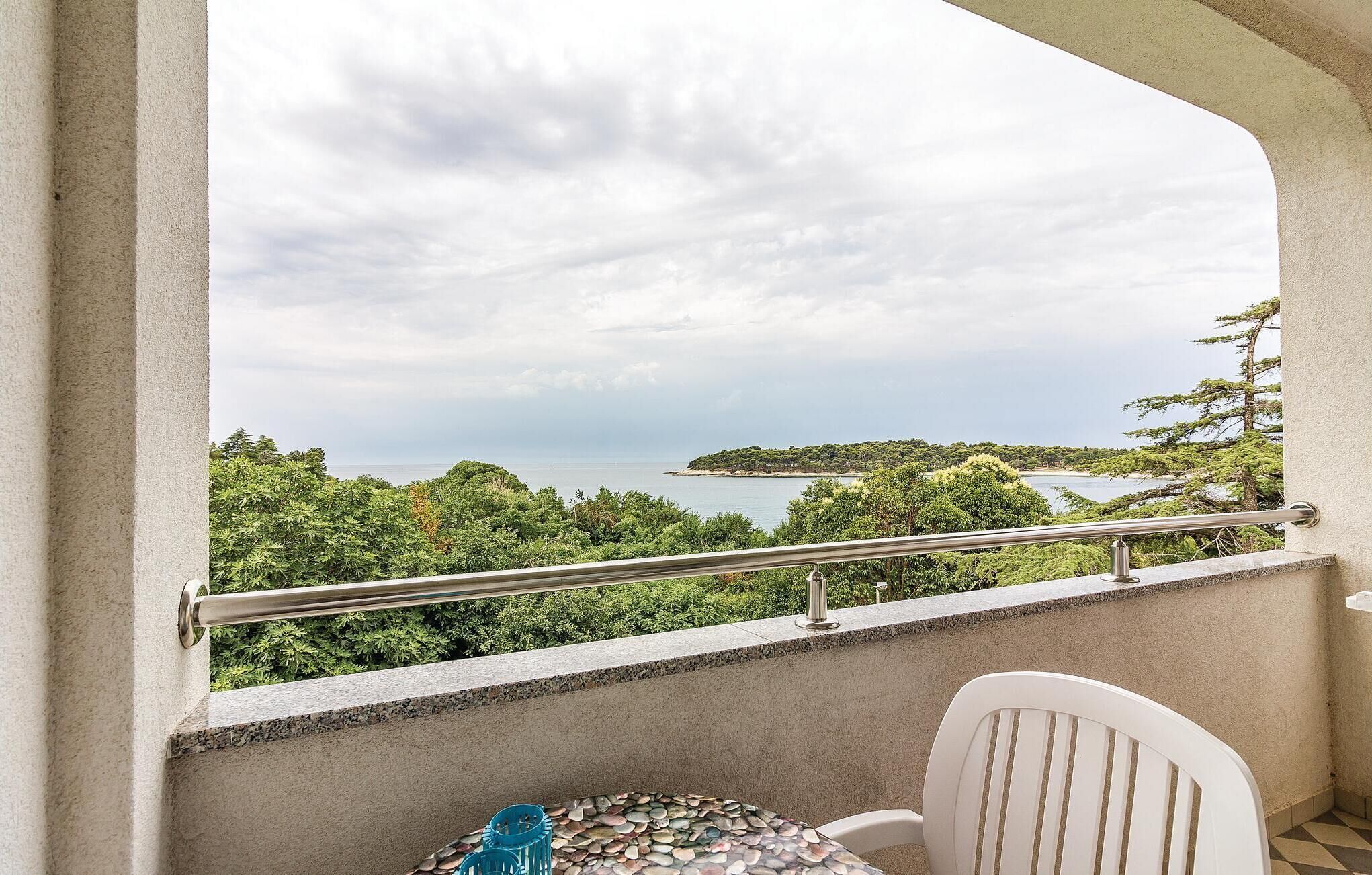 A balcony with a view of a coastal landscape, a table with chairs, and a railing.