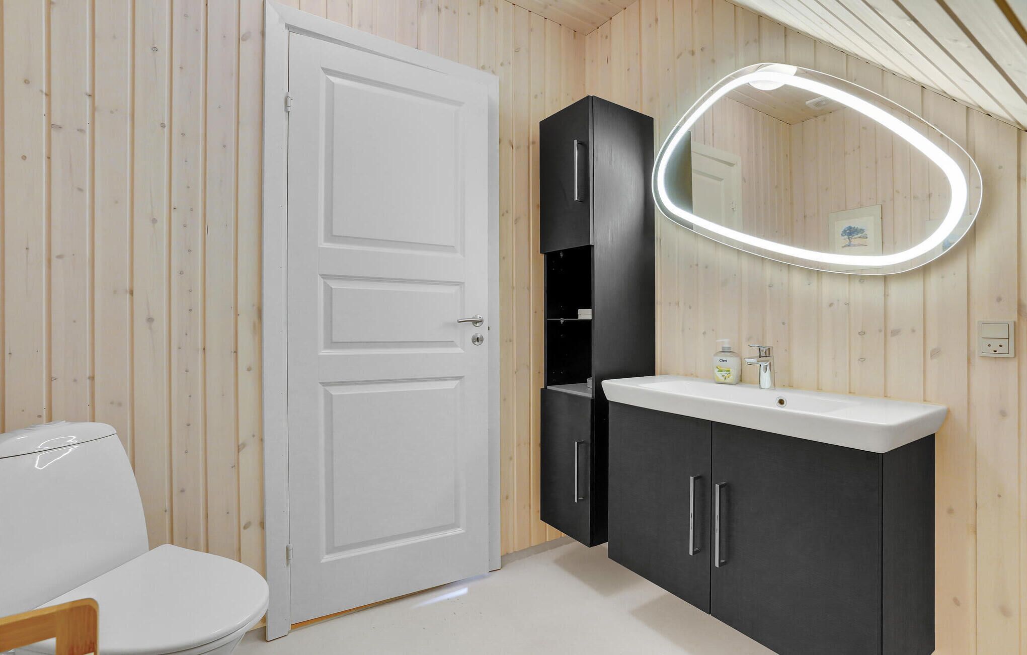 Ein Badezimmer mit Toilette, Waschbecken mit Spiegel und schwarzem Unterschrank.