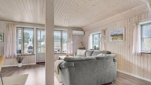 A cozy room with a grey sofa, wooden floors, large windows, and a ceiling fan.