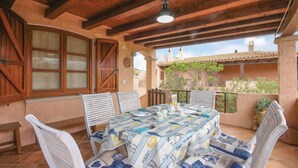 Un patio techado con una mesa lista para comer, rodeado de sillas blancas y un techo de madera.