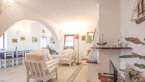 Una sala de estar acogedora con un sofá blanco, una mesa de comedor con sillas y una estantería decorativa con plantas y un telescopio.