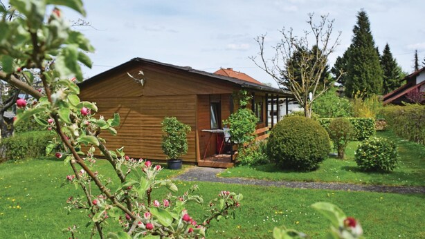 A wooden cabin with a porch, surrounded by a well-maintained garden with various shrubs and a lawn. - 2 bedroom nice home in Oberelbert (Oberelbert)