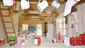 A cozy cabin interior with a wooden interior, a TV mounted on the wall, a dining table with chairs, and a kitchen area with a stove. - 2 bedroom amazing home in Væggerløse (Væggerløse)