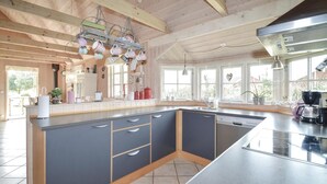 A modern kitchen with a large island, wooden ceiling beams, and large windows. - 2 bedroom amazing home in Væggerløse (Væggerløse)