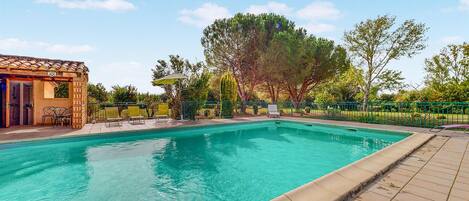 A swimming pool with a tiled deck, a covered seating area, and a pergola.