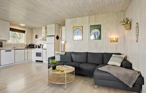 A modern kitchen with white cabinetry, a dining area with a dark grey sofa, and a round wooden coffee table. - Nice home in Thyholm with WiFi (Thyholm)