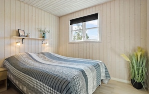 A bedroom with a bed, wooden walls, a window, a shelf with decorative items, and a bedside lamp. - Nice home in Thyholm with WiFi (Thyholm)