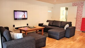 Una sala de estar moderna con un televisor de pantalla plana montado en la pared, una mesa de centro de madera, dos sofás grises con cojines blancos y un mueble de almacenamiento rojo.