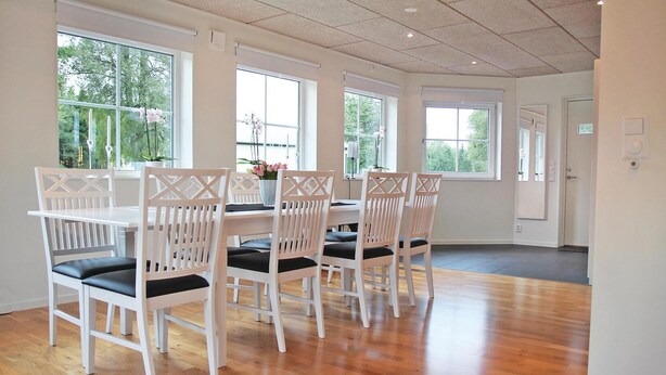 Un comedor con sillas blancas, una mesa, ventanas amplias y suelo de madera.