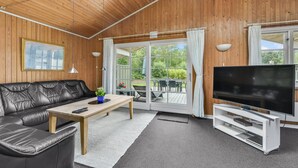 A cozy living room with a leather sofa, a coffee table, a TV on a white stand, and a large window with curtains.