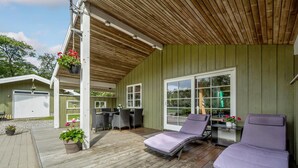 A covered outdoor patio with two lounge chairs, a table, and a hanging flower basket.