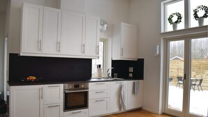 A modern kitchen with white cabinets, a black backsplash, stainless steel appliances, and a large window with a view of the outdoors. - Nice home in Borgholm with WiFi (Borgholm)