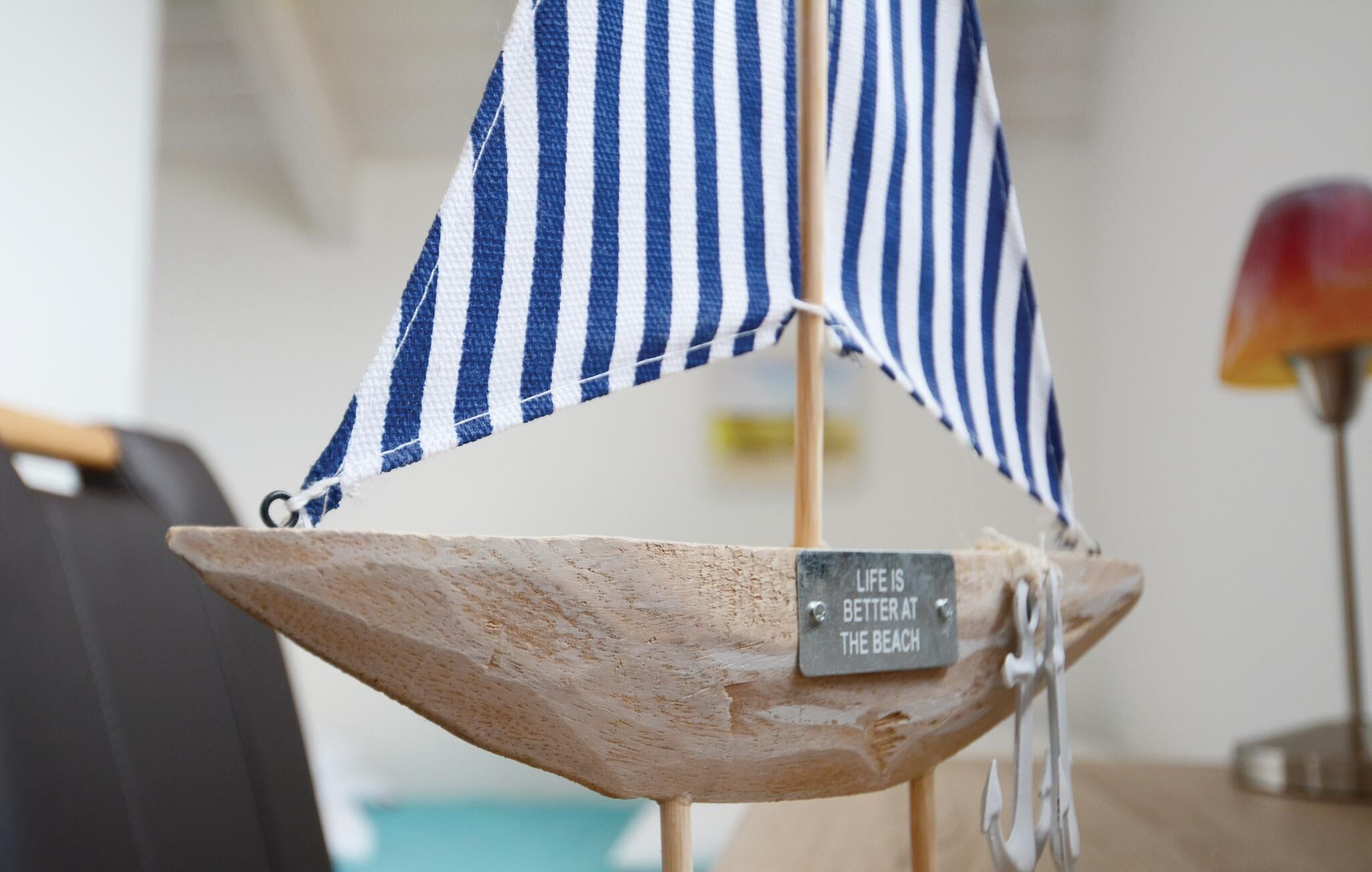A small wooden boat with a blue and white striped sail and a sign that reads "LIFE IS BETTER AT THE BEACH".